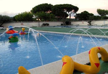 Piscina infantil con juguetes acuáticos coloridos y fuentes en un alojamiento glamping al atardecer.