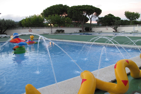 Piscina per bambini con giocattoli acquatici colorati e fontane in una struttura glamping al tramonto.