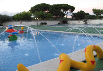Piscina per bambini con giocattoli acquatici colorati e fontane in una struttura glamping al tramonto.