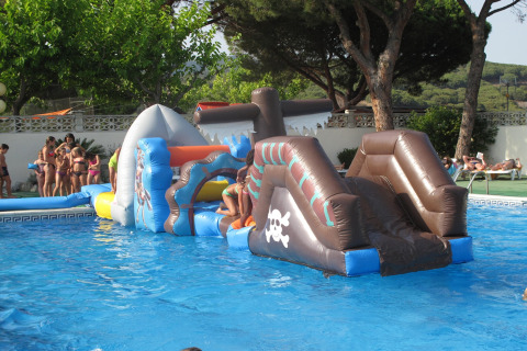 Bambini giocano su un percorso gonfiabile in piscina presso un alloggio glamping con alberi intorno.