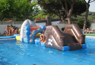 Bambini giocano su un percorso gonfiabile in piscina presso un alloggio glamping con alberi intorno.