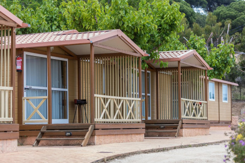 Holz-Bungalow für 5 Personen im Camping Rocagrossa, Spanien, umgeben von Bäumen und Natur.