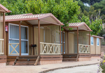 Wooden bungalow for 5 people at Camping Rocagrossa in Spain, surrounded by greenery and trees.