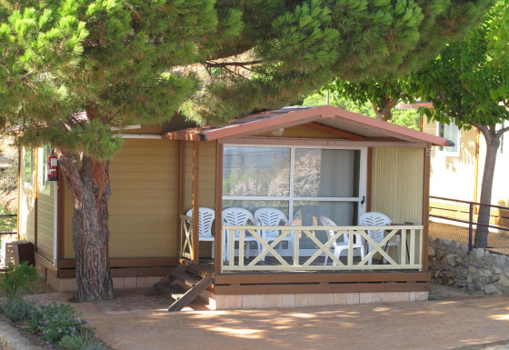 Holzbungalow im Camping Rocagrossa für 5 Personen, Terrasse mit Stühlen und großen schattigen Bäumen.