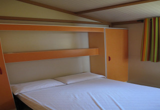 Soveværelse på Camping Rocagrossa Bungalow for 4 personer i Spanien med dobbeltseng og farverige gardiner.