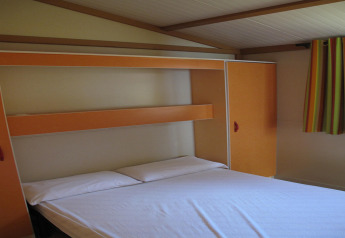 Bedroom at Camping Rocagrossa Bungalow for 4 people in Spain, featuring a double bed and striped curtains.