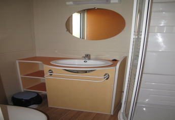 Bathroom in Camping Rocagrossa Bungalow for 4 people in Spain, features sink, mirror, shelves, and shower.