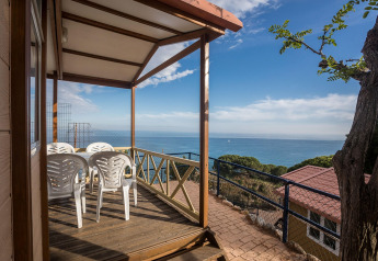 Covered deck with white chairs and stunning sea view at Camping Rocagrossa Bungalow 4 people in Spain.
