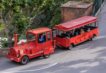 Small red tourist train with passengers driving on a road at a glamping accommodation in nature.
