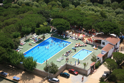 Luftfoto af Camping Rocagrossa med to swimmingpools, solstole og omgivet af frodige træer i Spanien.