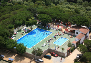 Luftfoto af Camping Rocagrossa med to swimmingpools, solstole og omgivet af frodige træer i Spanien.