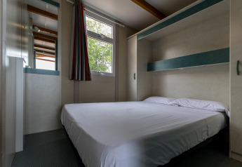 Bedroom with double bed and modern decor at Camping Rocagrossa Bungalow for 5 people in Spain.