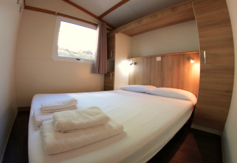 Chambre douillette avec lit double, éléments en bois et serviettes propres au Camping Rocagrossa Bungalow en Espagne.