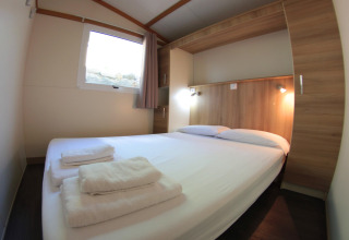 Gemütliches Schlafzimmer mit Doppelbett, Holzdetails und frischen Handtüchern im Camping Rocagrossa Bungalow in Spanien.