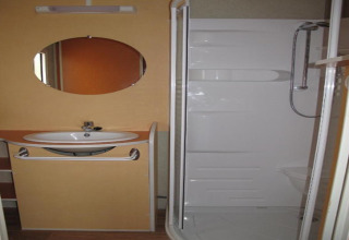 Badezimmer im Camping Rocagrossa Bungalow in Spanien mit Waschbecken, Spiegel und moderner Dusche.