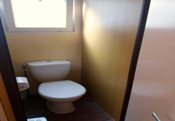 Petite salle de bain avec WC blanc, fenêtre et porte fermée au Camping Rocagrossa en Espagne.