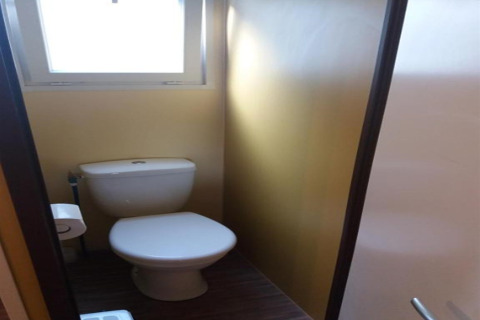 Lille badeværelse med et toilet, et vindue til dagslys og en lukket dør i Camping Rocagrossa, Spanien.
