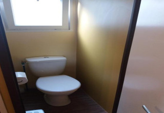 Lille badeværelse med et toilet, et vindue til dagslys og en lukket dør i Camping Rocagrossa, Spanien.