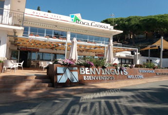 Photo de l’hébergement glamping Roca Grossa avec panneau de bienvenue, restaurant et terrasse ensoleillée.