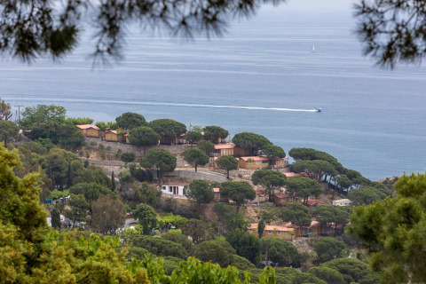 Blick auf Lodges zwischen Bäumen am Meer, mit einem Boot und einem Segelboot im Hintergrund.