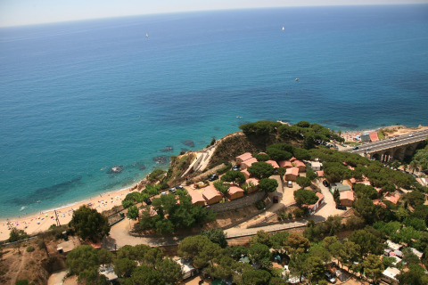 Luftaufnahme von Glamping-Hütten an einer Küste, umgeben von Bäumen, mit Blick auf das blaue Meer.