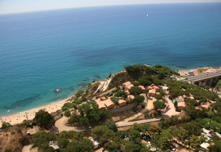 Vista aerea di tende glamping sulla costa, immerse nel verde, con vista su spiaggia e mare azzurro.