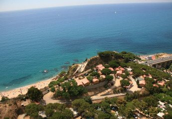 Aerial view of Camping Rocagrossa Bungalow in Spain, overlooking the sea, sandy beach, and lush greenery.