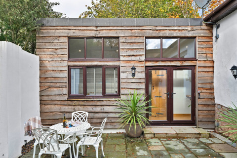 Udendørs terrasse ved Hillfarrow Hideaway-hytte i Storbritannien med træbeklædning og havemøbler.