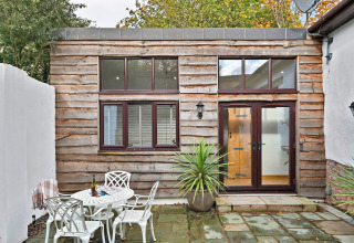 Udendørs terrasse ved Hillfarrow Hideaway-hytte i Storbritannien med træbeklædning og havemøbler.