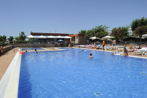 Piscina al aire libre en un alojamiento glamping con personas nadando y tomando el sol en tumbonas.