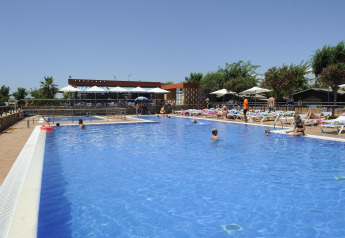 Outdoor pool at a glamping site with guests swimming and sunbathing on loungers under clear blue sky.