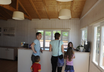 Famille s'enregistrant à la réception d’un hébergement glamping avec murs en bois et ambiance chaleureuse.