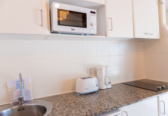 Modern white kitchen at Camping del Mar BUNGALOW MEDITERRANI in Spain with microwave, toaster, and stove.