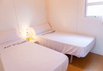 Two twin beds in a bright room at Camping del Mar BUNGALOW MEDITERRANI in Spain, featuring a window and nightstand.