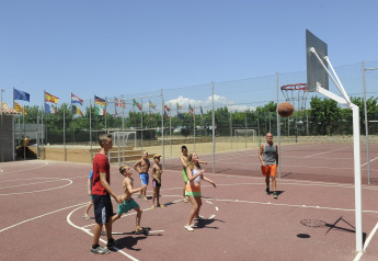 Des enfants et des adultes jouent au basket sur un terrain extérieur dans un hébergement glamping, drapeaux visibles.