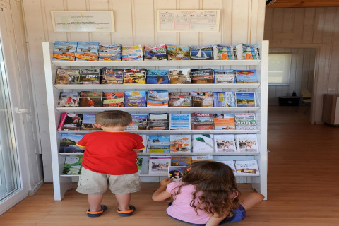 Twee kinderen bekijken folders bij een rek in Camping del Mar BUNGALOW MEDITERRANI in Spanje.