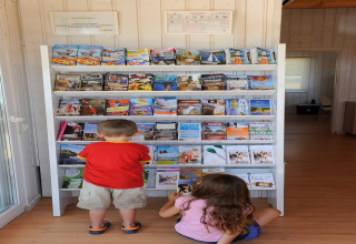 Twee kinderen bekijken folders bij een rek in Camping del Mar BUNGALOW MEDITERRANI in Spanje.