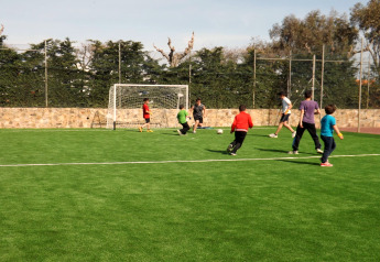Kinder und Erwachsene spielen Fußball auf einem Sportplatz bei einer Glamping-Unterkunft im Grünen.
