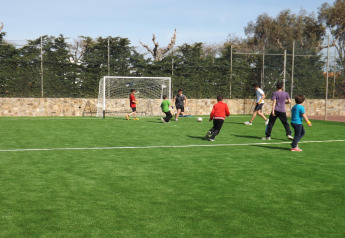 Des enfants et des adultes jouent au football sur un terrain vert dans un hébergement glamping en pleine nature.