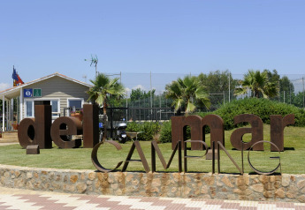 Entrada al Del Mar Camping con letras metálicas grandes, palmeras y una caseta, ideal para glamping.