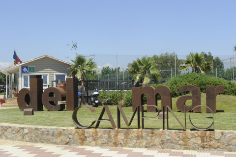 Entrée du Del Mar Camping avec de grandes lettres métalliques, palmiers et un petit bâtiment, idéal pour glamping.
