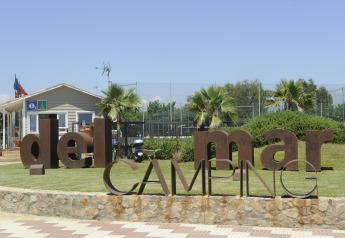 Entrada al Del Mar Camping con letras metálicas grandes, palmeras y una caseta, ideal para glamping.