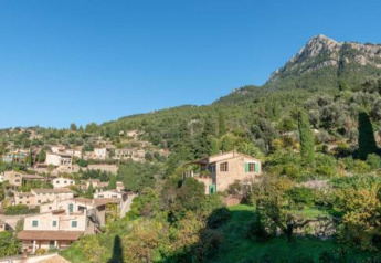 Mountainous landscape with stone lodges and green hills under a clear blue sky near Camping del Mar, Spain.