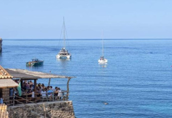 View from Camping del Mar BUNGALOW MEDITERRANI in Spain with boats on the sea and people dining on a terrace.