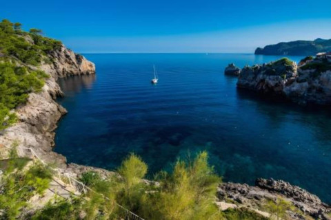 Prachtig uitzicht op een rustige baai met zeilboot, rotsen en helderblauw water bij Camping del Mar BUNGALOW MEDITERRANI in Spanje.