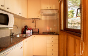 Cocina luminosa con paneles de madera, ventana amplia, fogón, microondas y cafetera en una cabaña española.