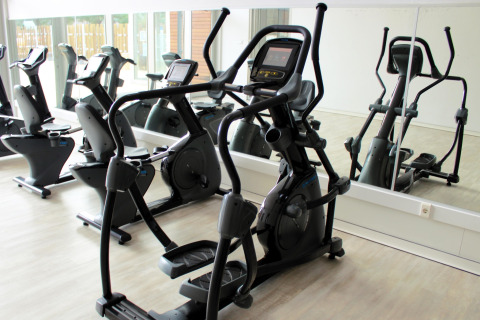 Sala de fitness en glamping con máquinas elípticas y bicicletas estáticas junto a una pared de espejos.