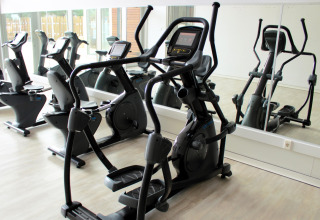 Sala de fitness en glamping con máquinas elípticas y bicicletas estáticas junto a una pared de espejos.