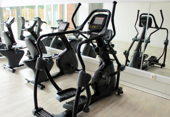 Sala de fitness en glamping con máquinas elípticas y bicicletas estáticas junto a una pared de espejos.