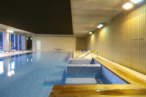 Piscina cubierta en alojamiento glamping, con jacuzzi, tumbonas y paredes de madera bajo iluminación.